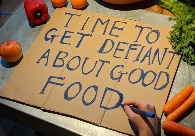 Hand writing a sign that says 'time to get defiant about good food'