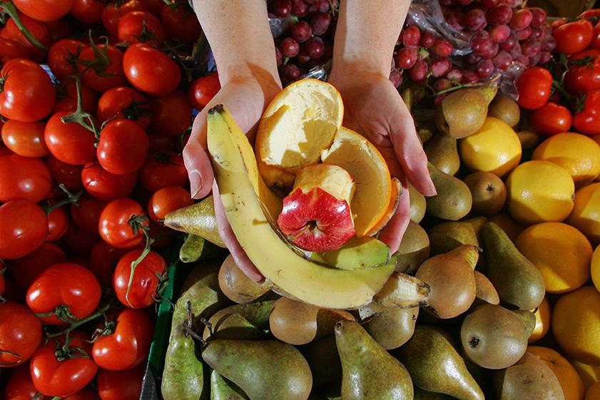 Hands holding fruit peelings with fresh fruit stall as background
